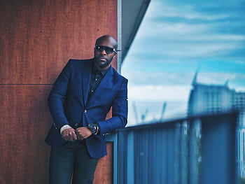 A fashionable man in a blue suit poses on a city balcony, exuding elegance. HD wallpaper
