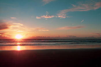 A tranquil beach sunset with vivid colors reflecting on the sand and sea, capturing a peaceful seascape. HD wallpaper