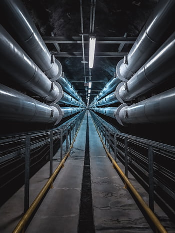 A dramatic view of a symmetric industrial tunnel lined with steel pipes. HD phone wallpaper