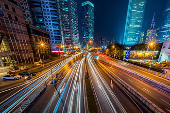 Dynamic long exposure night shot of urban cityscape with vibrant light trails and towering skyscrapers. HD wallpaper