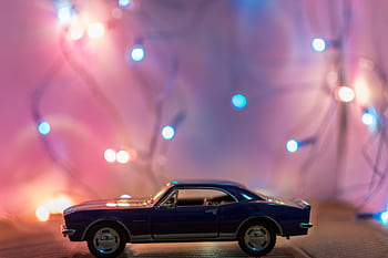 A miniature toy car in front of colorful festive lights creating a bokeh effect. HD wallpaper