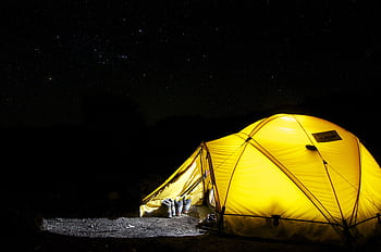 A glowing yellow tent pitched outdoors under a vast, star-filled night sky, capturing the essence of camping adventure. HD wallpaper