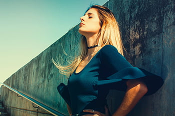 Fashionable woman posing with closed eyes against concrete wall, sunny day. HD wallpaper