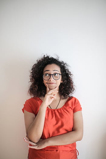 Portrait of a thoughtful woman in a red top, with curly hair and glasses against a white background. HD phone wallpaper
