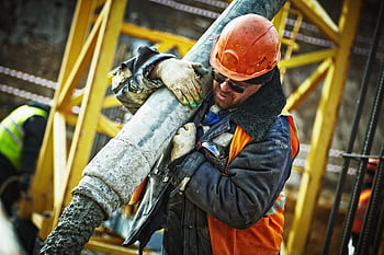 Construction worker in safety gear handling equipment on an active site. HD wallpaper
