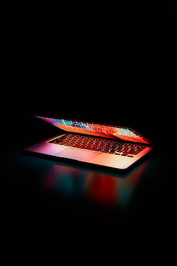 Laptop partially opened, emitting vibrant multicolored lights in dark setting. HD phone wallpaper