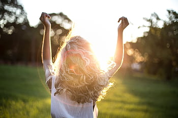 A woman with outstretched arms celebrates the sunset in a grassy field, capturing the essence of dom and joy. HD wallpaper