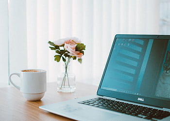 Comfortable home office desk with laptop, coffee mug, and flower vase. HD wallpaper