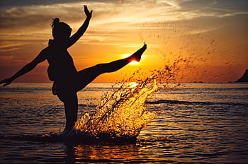 Silhouette of a woman splashing water with a kick against a stunning sunset over the ocean. HD wallpaper