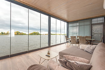 Spacious and modern living room with glass walls offering a serene lake view. Perfect for relaxation. HD wallpaper