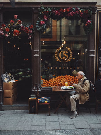 A que street café in Stockholm featuring an elderly man enjoying a meal outside a beautifully decorated shop display. HD phone wallpaper