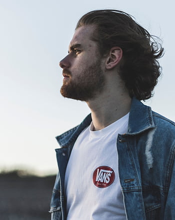 Profile of a fashionable man in a denim jacket outdoors, exuding a serious demeanor. HD phone wallpaper
