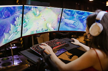 A young woman intently gaming on a multi-screen setup, showcasing vibrant gaming visuals. HD wallpaper