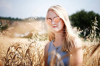 Blonde woman in sunglasses standing in a sunny wheat field. HD wallpaper