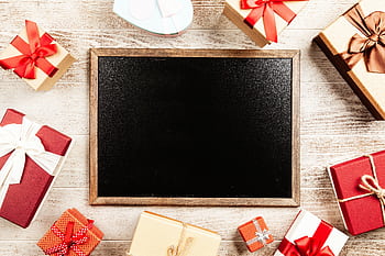 Flat lay of colorful gift boxes with ribbons surrounding a blank blackboard for holiday season messaging. HD wallpaper