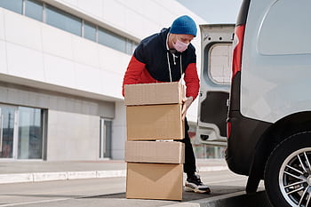 Delivery worker wearing a face mask loads boxes into a van, reflecting pandemic precautions. HD wallpaper