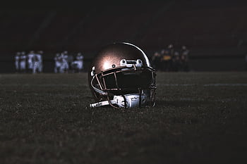 A football helmet placed on a grassy field during a nighttime game, capturing the spirit of sports. HD wallpaper