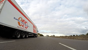 A large semi truck labeled 'Supply Chain Solutions' travels down a highway under a cloudy sky. HD wallpaper