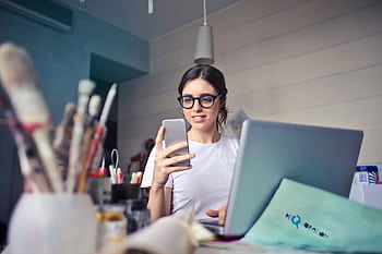 A woman using her at a desk, surrounded by art supplies and a laptop, in a creative workspace. HD wallpaper