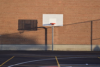 Empty outdoor basketball court with hoop and shadow against brick wall HD wallpaper