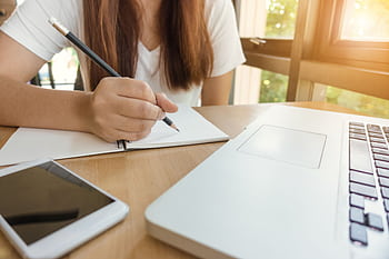 A young woman writing notes at a table with laptop and smart. HD wallpaper