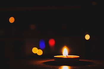A candle glows warmly in the foreground against a bokeh-filled dark background. HD wallpaper