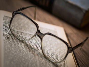 Close-up of a pair of eyeglasses resting on an open book, emphasizing reading and knowledge. HD wallpaper