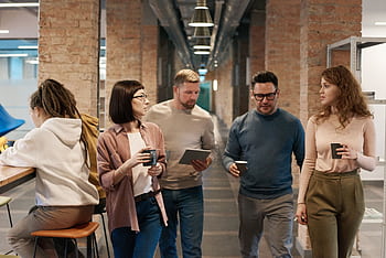 A diverse group of colleagues discussing a project in a modern office hallway. HD wallpaper