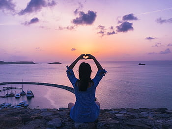 A woman forms a heart shape with her hands against a colorful sunset over the sea in Saint Martin. HD wallpaper