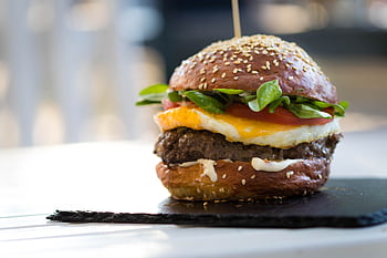 Close-up of a gourmet cheeseburger with spinach and fried egg on a sesame bun. HD wallpaper
