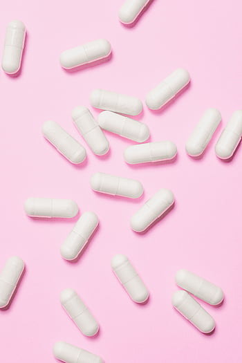 White medicinal capsules scattered on a vibrant pink background, symbolizing healthcare and wellness. HD phone wallpaper