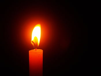A single candle flame illuminating the darkness, symbolizing warmth and hope. HD wallpaper