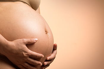 A tender close-up of a pregnant woman's hands holding her belly, symbolizing maternity and love. HD wallpaper
