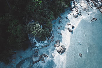 Aerial shot of a rocky beach with turquoise water and lush green forest. HD wallpaper