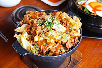 Savory Korean stir-fried noodles with vegetables and meat in a traditional stone bowl. HD wallpaper