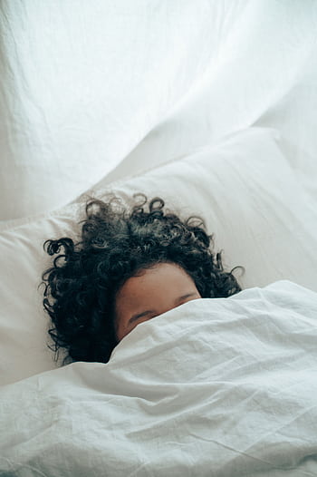 A person with curly hair sleeping peacefully under a white blanket, creating a sense of calm. HD phone wallpaper
