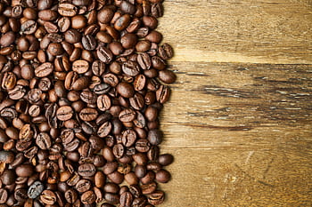 A heap of aromatic coffee beans on a rustic wooden table. HD wallpaper