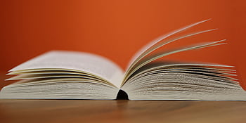 An open book with pages turning against a vibrant orange background, symbolizing knowledge and education. HD wallpaper