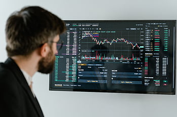 A businessman in a suit looks at a screen displaying stock market charts and data analysis. HD wallpaper