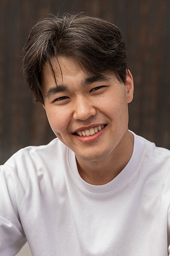 Cheerful young man with a toothy smile wearing a white t-shirt and posing confidently outdoors. HD phone wallpaper
