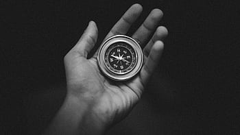Black and white of a hand holding a compass, conveying direction and exploration. HD wallpaper