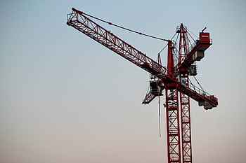 A red tower crane on a construction site set against a clear sky during daytime. HD wallpaper