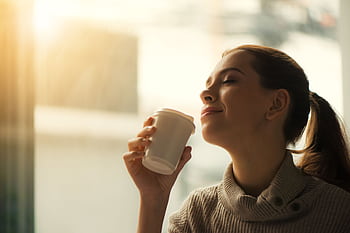Smiling woman savoring morning coffee by the window in soft warm light. HD wallpaper