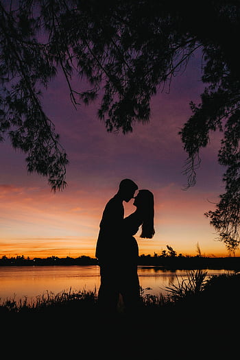 A couple embraces in a romantic silhouette by the lake during a vibrant sunset. HD phone wallpaper