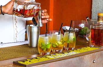 Bartender pouring rum into cocktail glasses at a vibrant bar setting. HD wallpaper