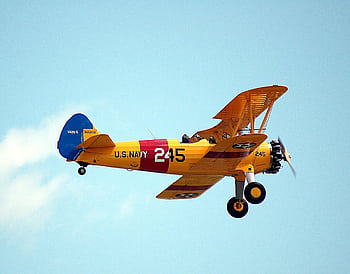 A vintage U.S. Navy biplane flying against a clear blue sky, showcasing classic aviation design. HD wallpaper