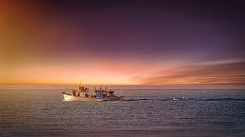 A serene of a fishing boat navigating a calm sea at sunset, with colorful skies. HD wallpaper