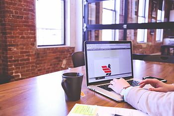 Person working on laptop in a trendy brick-walled office with modern aesthetics. HD wallpaper