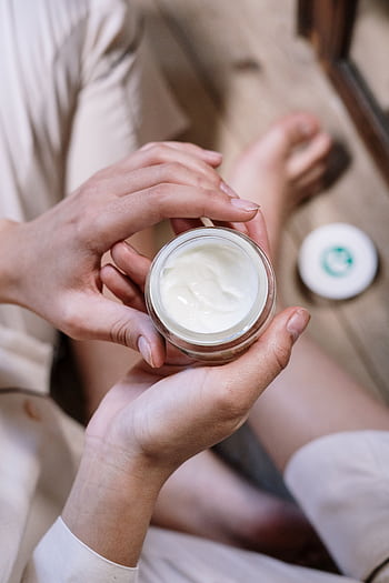 Close-up of woman's hands applying skincare cream during morning routine indoors. HD phone wallpaper