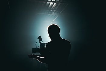 Silhouette of a cinematographer with camera gear in a dramatic, low light setting. HD wallpaper